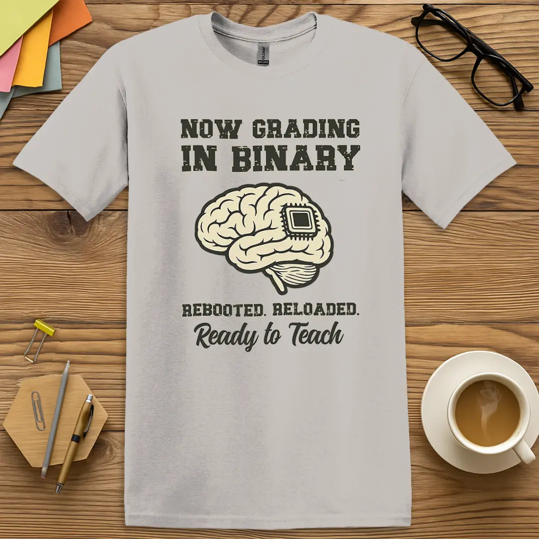 Ice Grey Color T-shirt with "Now Grading in Binary – Rebooted. Reloaded. Ready to Teach" design featuring a chip-brain graphic and teacher tech charm.