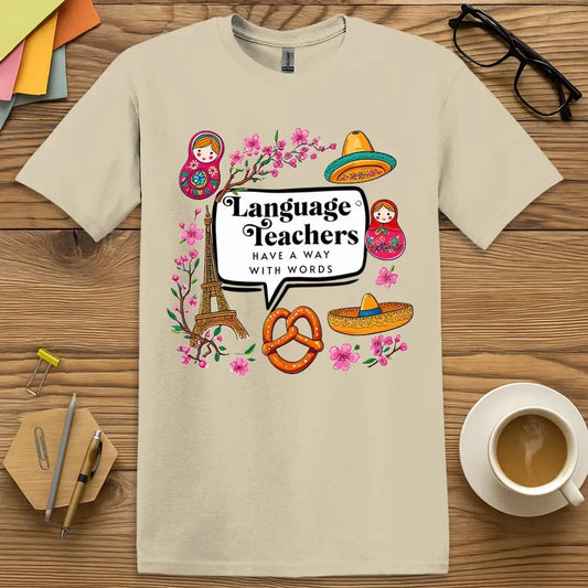 Sand Color T-shirt with "Language Teachers Have a Way With Words" design featuring Eiffel Tower, pretzel, sombrero, and matryoshka graphics.