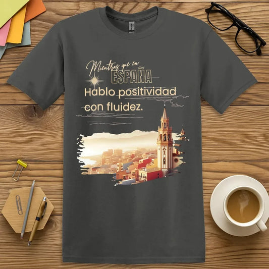 Charcoal T-shirt with “Mientras que en España, Hablo positivo con fluidez” design featuring witty bilingual positivity for Spanish lovers