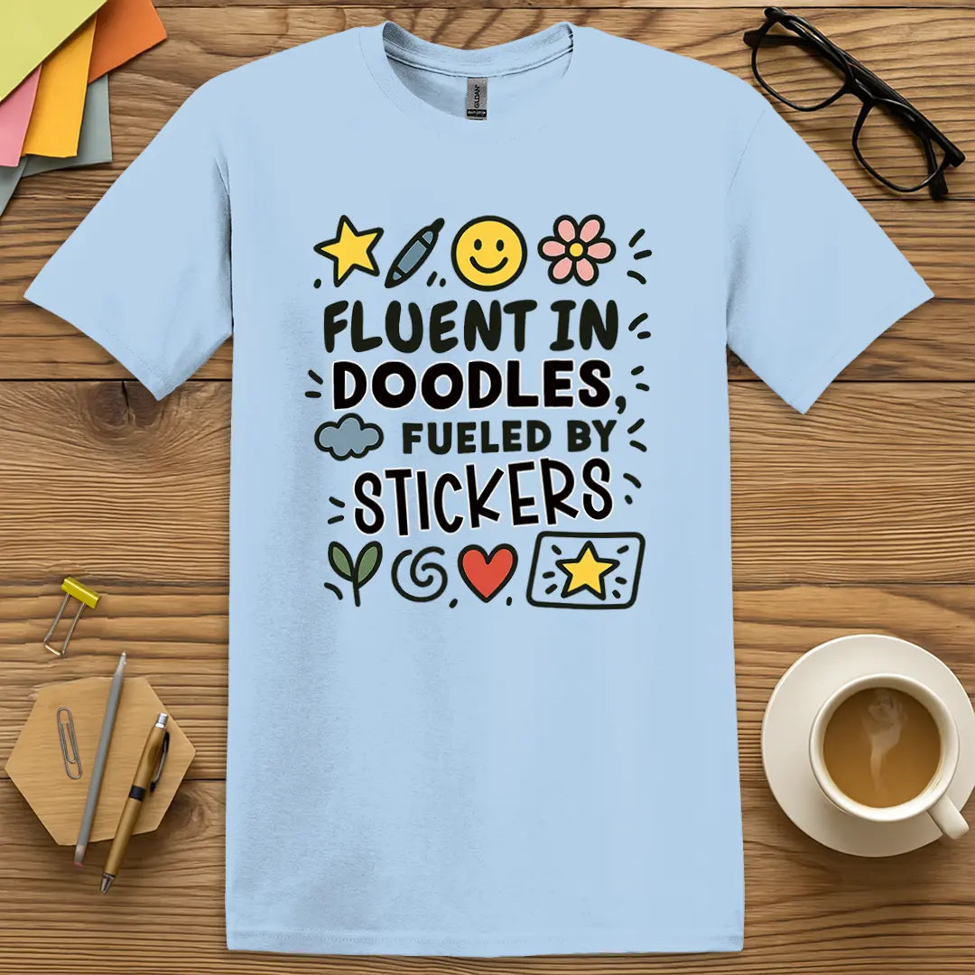 Light Blue Color T-shirt with "Fluent in Doodles, Fueled by Stickers" design evoking calm art class charm and imaginative vibes.