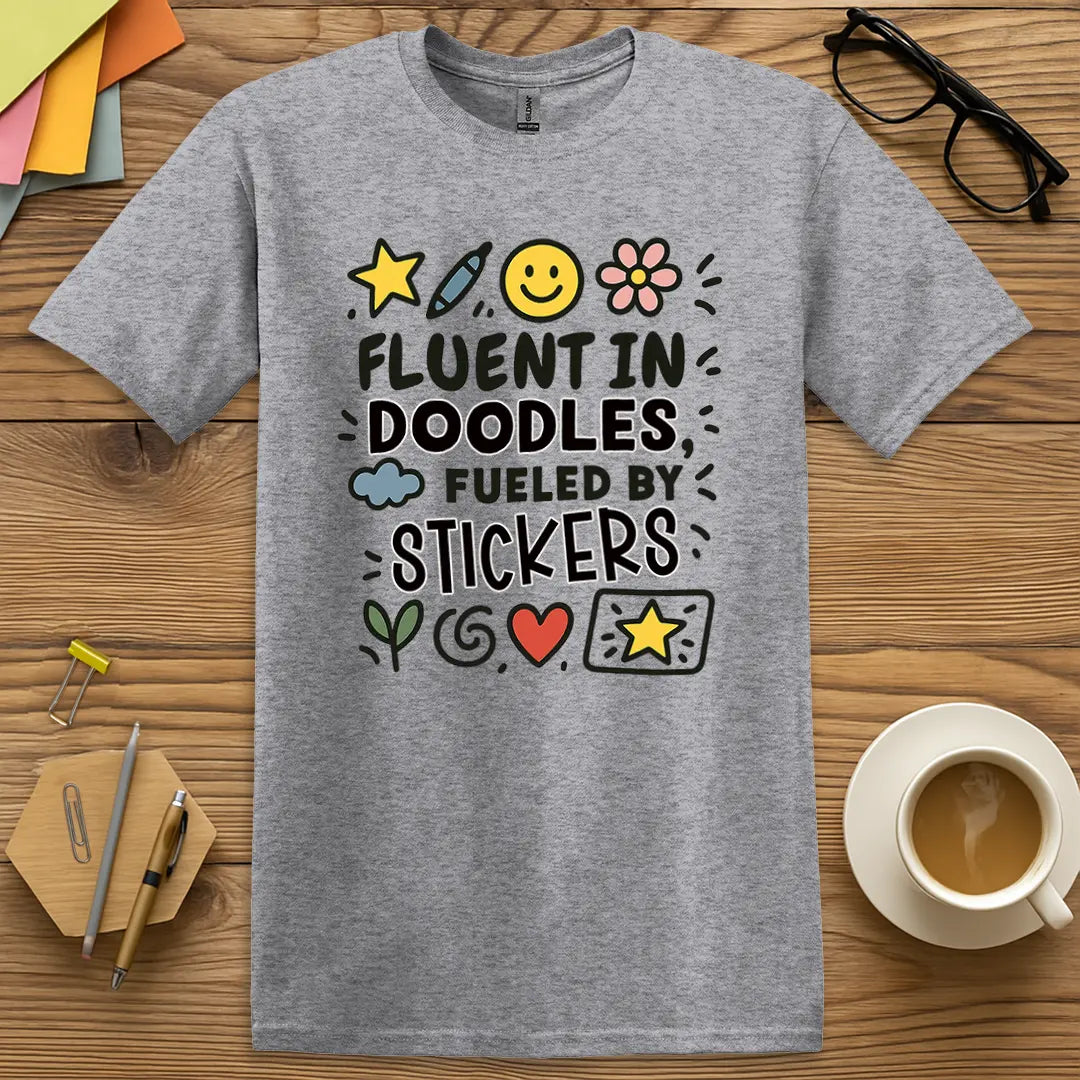 Sport Grey Color T-shirt with "Fluent in Doodles, Fueled by Stickers" design offering neutral base and expressive art teacher personality.
