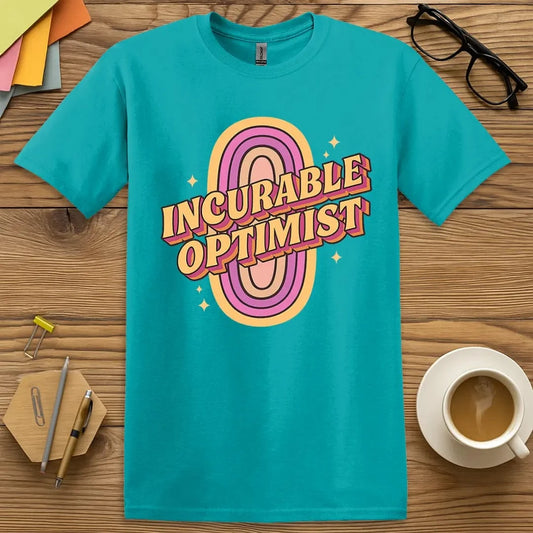 Tropical Blue T-shirt with “Incurable Optimist” design featuring bold retro typography and rainbow ovals bursting with positive teacher energy  